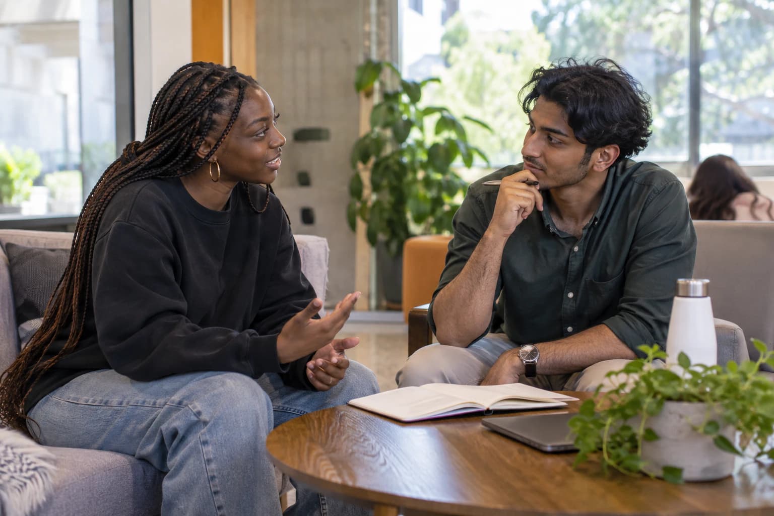 Two young adults having a focused mentoring conversation in a campus lounge.